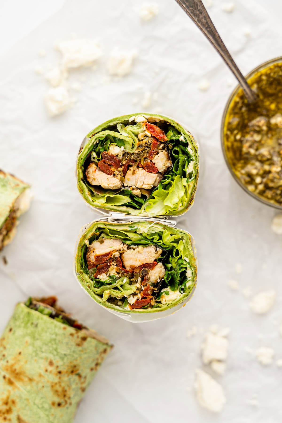 Spinach wraps with chicken, lettuce, and sundried tomatoes, sliced in half on parchment paper.