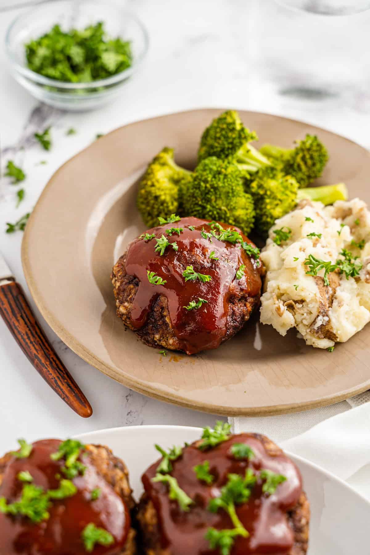 A plate with meatloaf, mashed potatoes, broccoli, and parsley garnish.