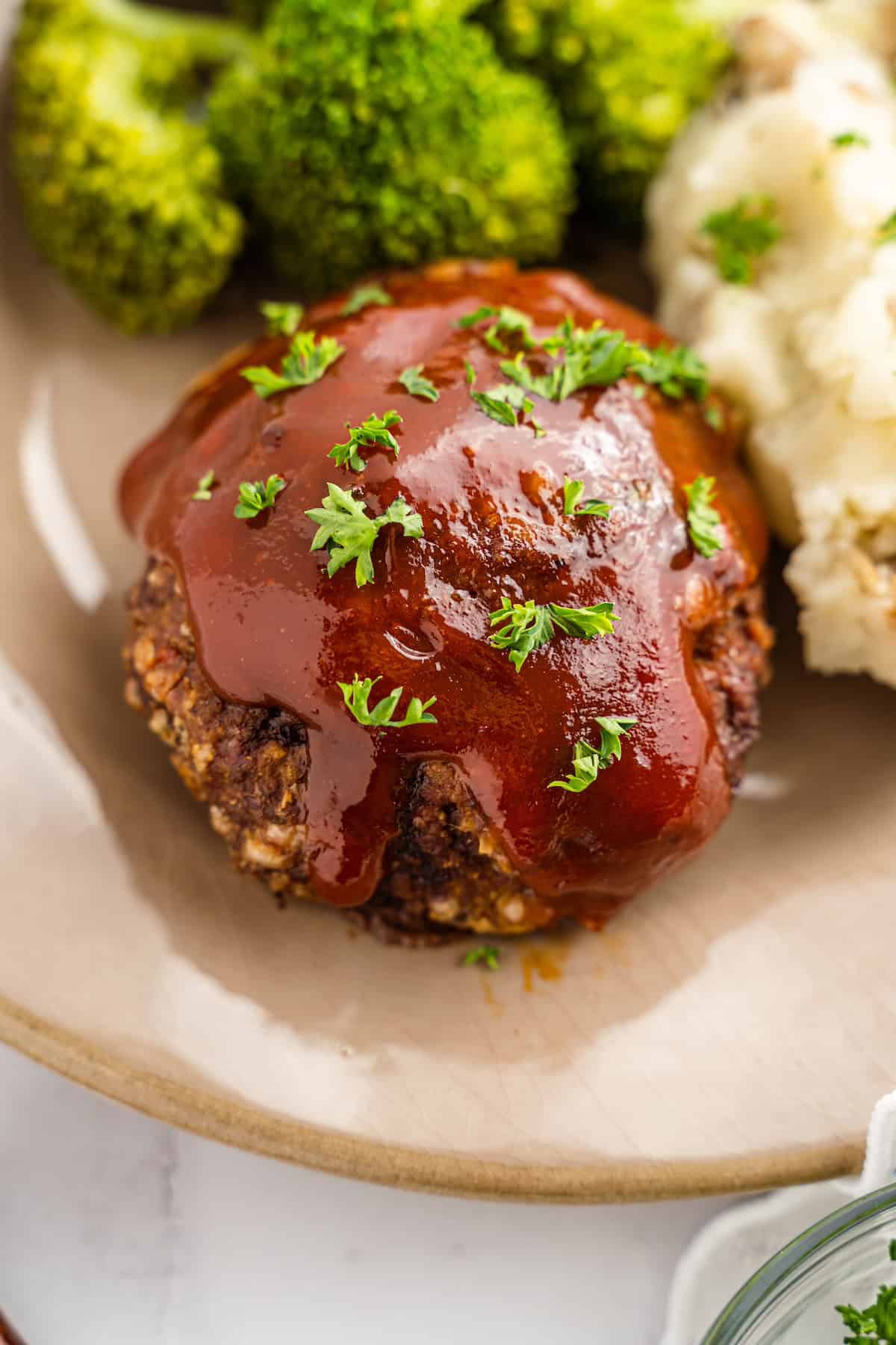 Mini meatloaf with ketchup glaze, mashed potatoes, and broccoli on a beige plate.