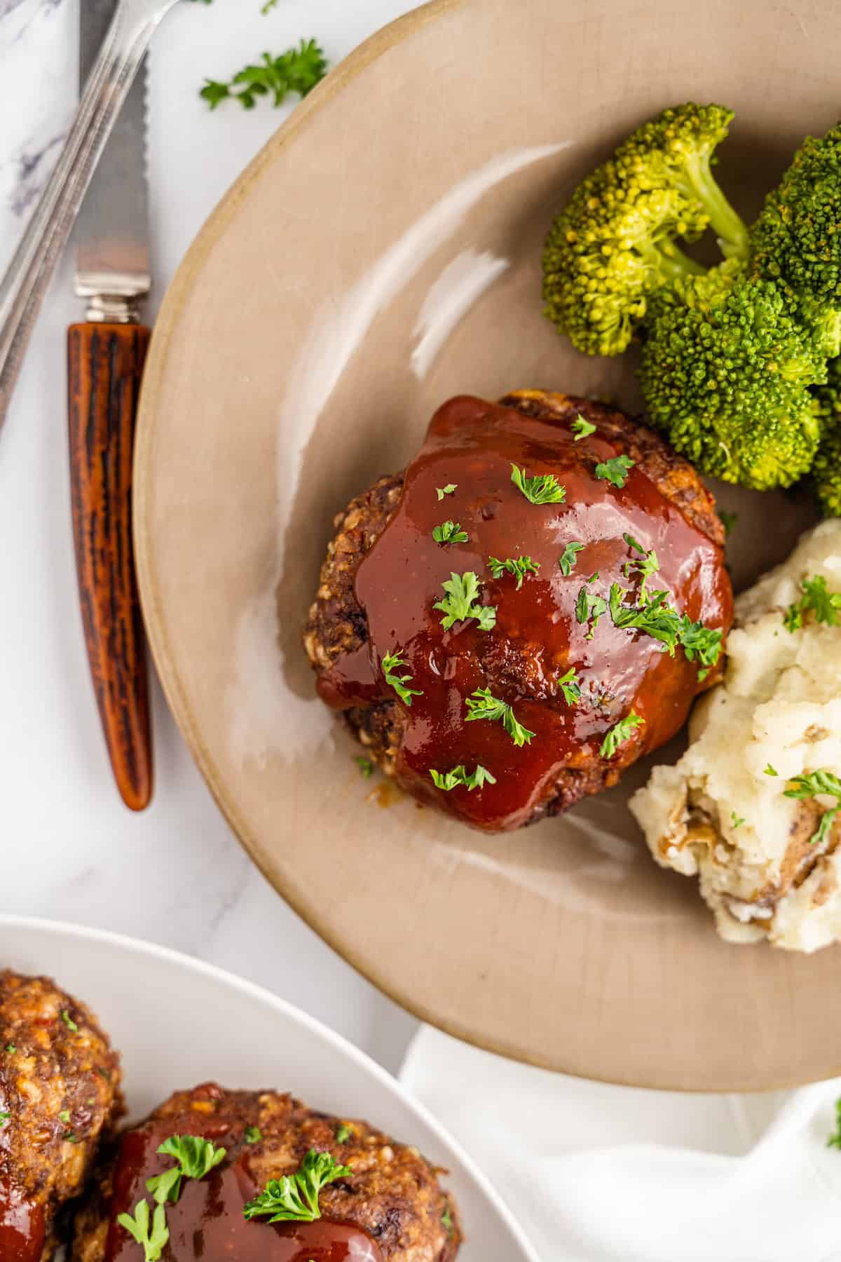 Plate with meatloaf topped with sauce, mashed potatoes, and broccoli, shot from above.