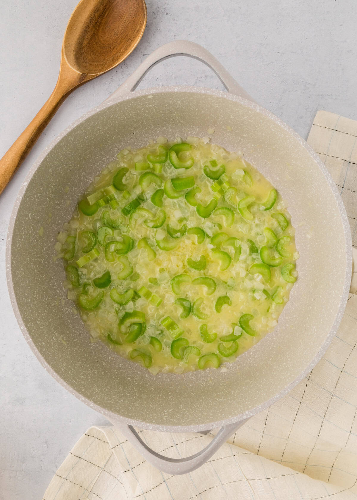 Sautéed onions and celery cooking in a pot with a wooden spoon beside it.