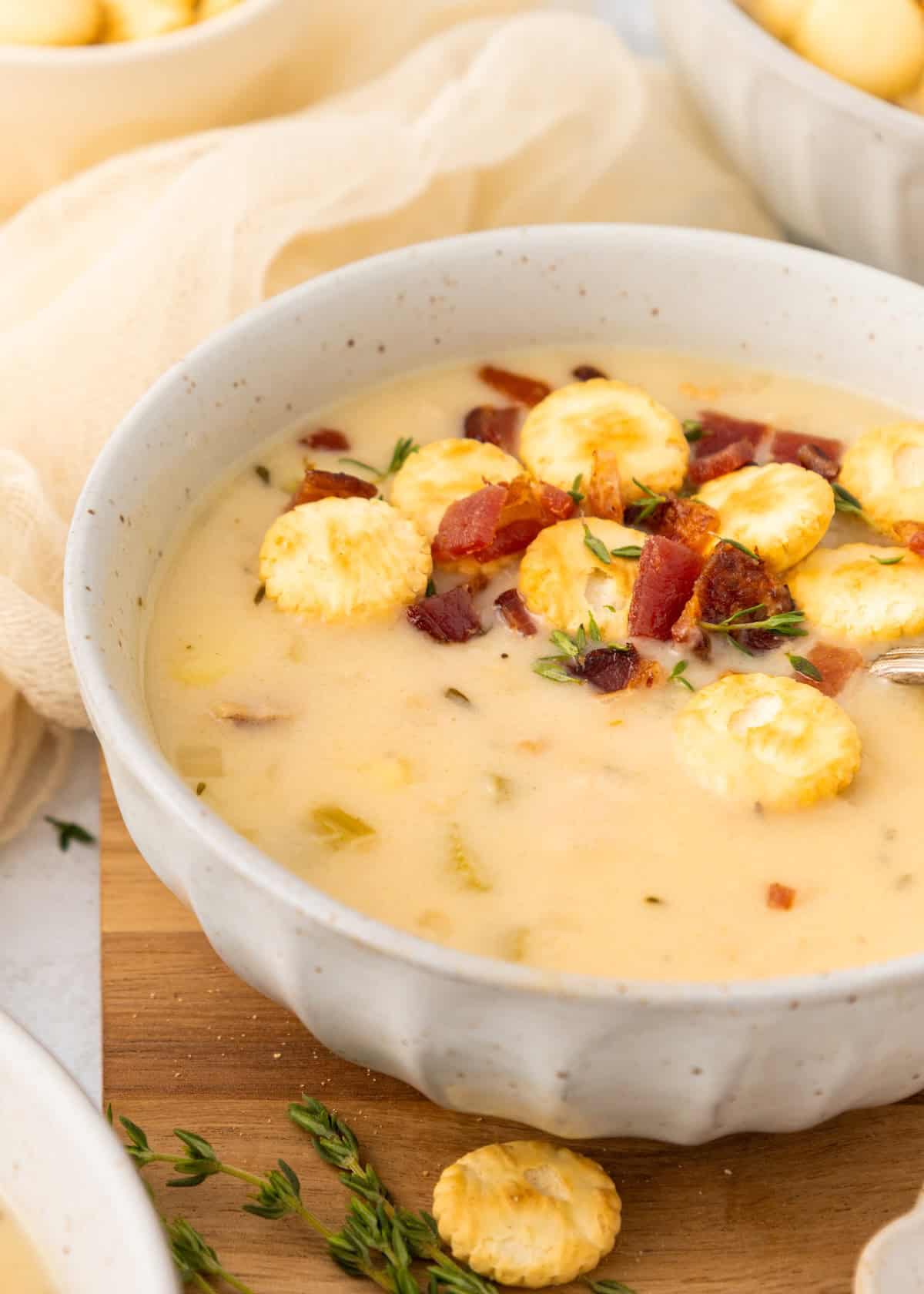 Creamy soup topped with oyster crackers, bacon bits, and fresh herbs in a white bowl.