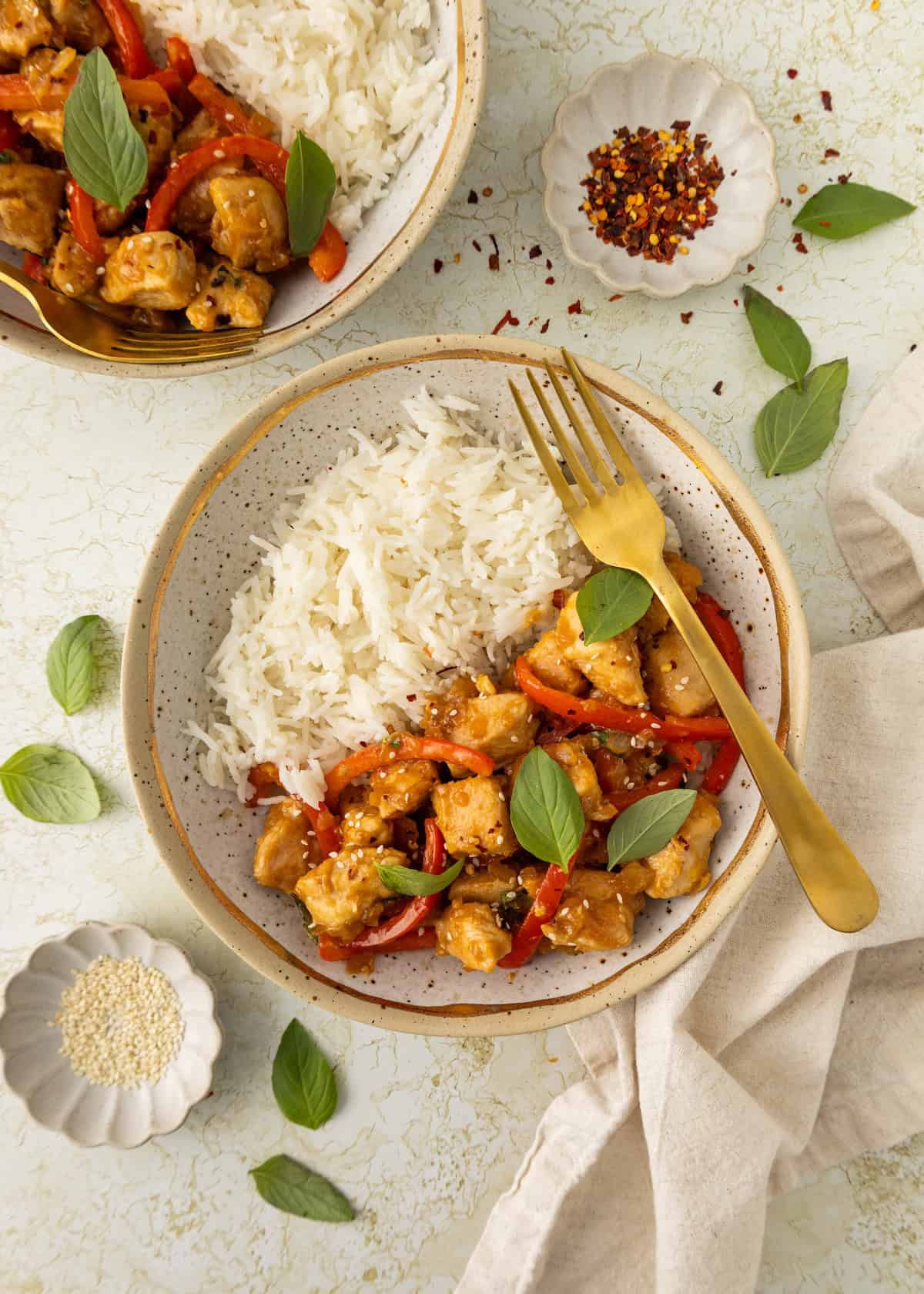 A plate of Thai Basil Chicken with white rice, red peppers, basil leaves, and a gold fork.