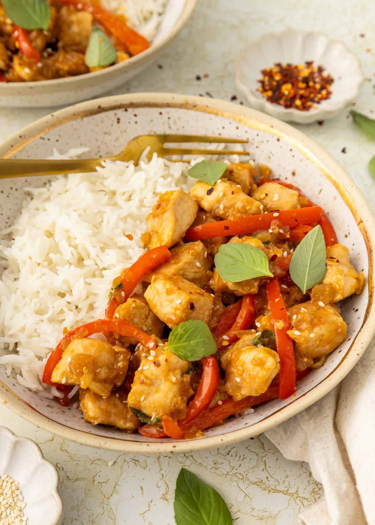 A bowl of rice with stir-fried Thai Basil Chicken, red peppers, and fresh basil leaves.