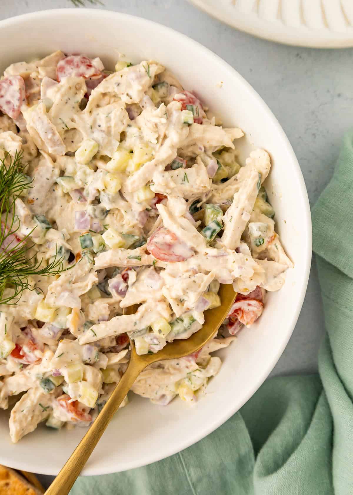 Bowl of creamy Tzatziki Chicken Salad with vegetables, gold spoon, and fresh dill garnish.