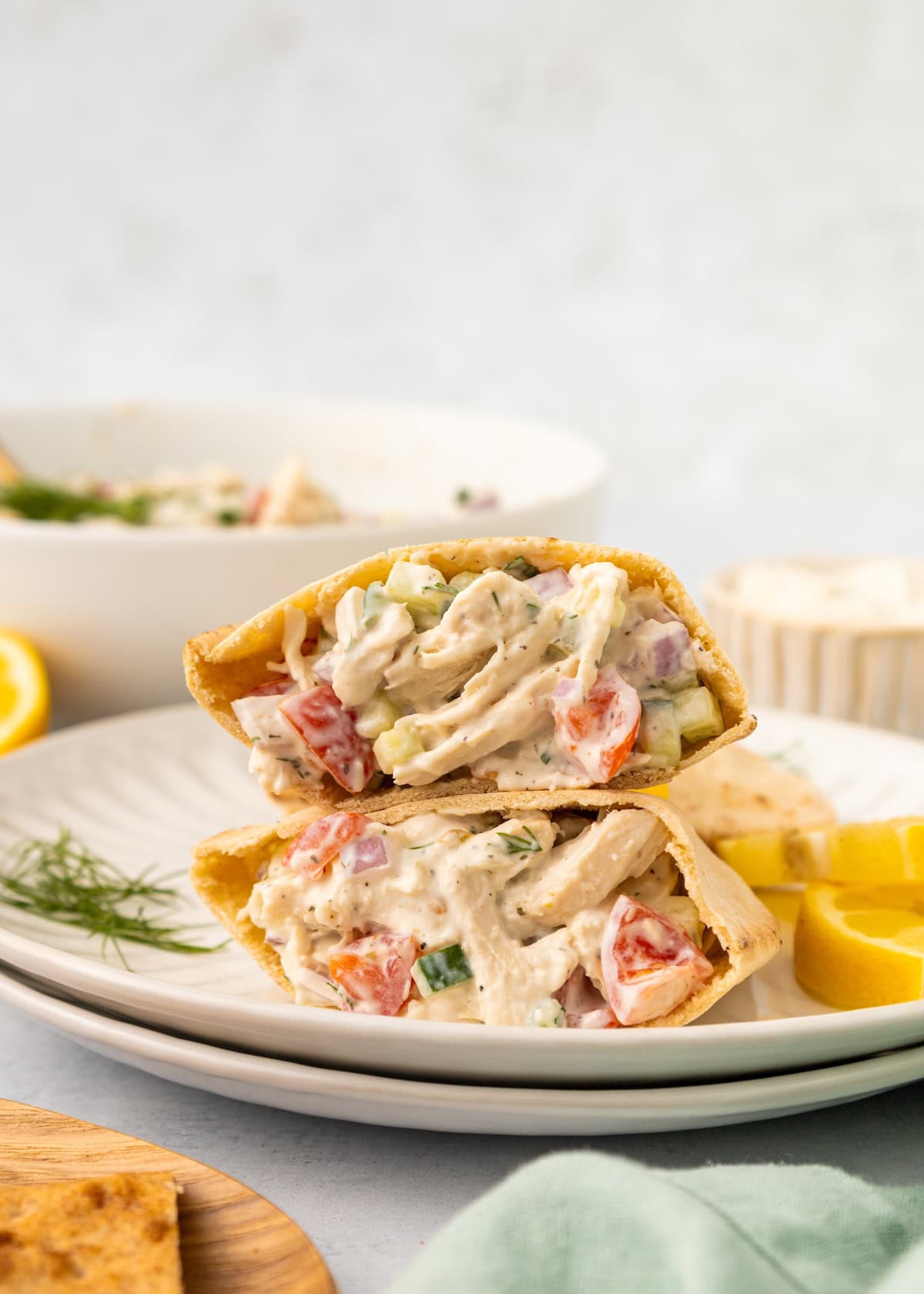 Pita sandwich halves filled with Tzatziki Chicken Salad, tomatoes, and herbs on a white plate.