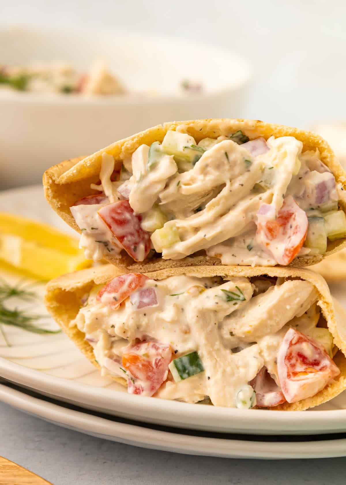 Tzatziki Chicken Salad with tomatoes and cucumbers stuffed in pita bread on a white plate.