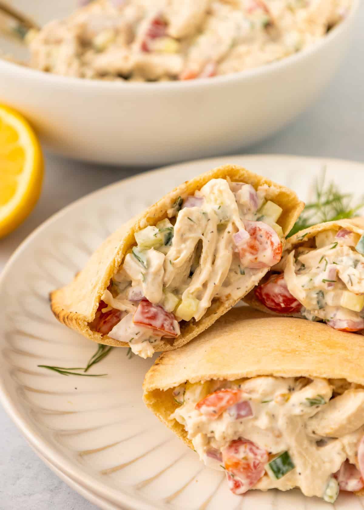 Pita bread stuffed with Tzatziki Chicken Salad and vegetables on a white plate.