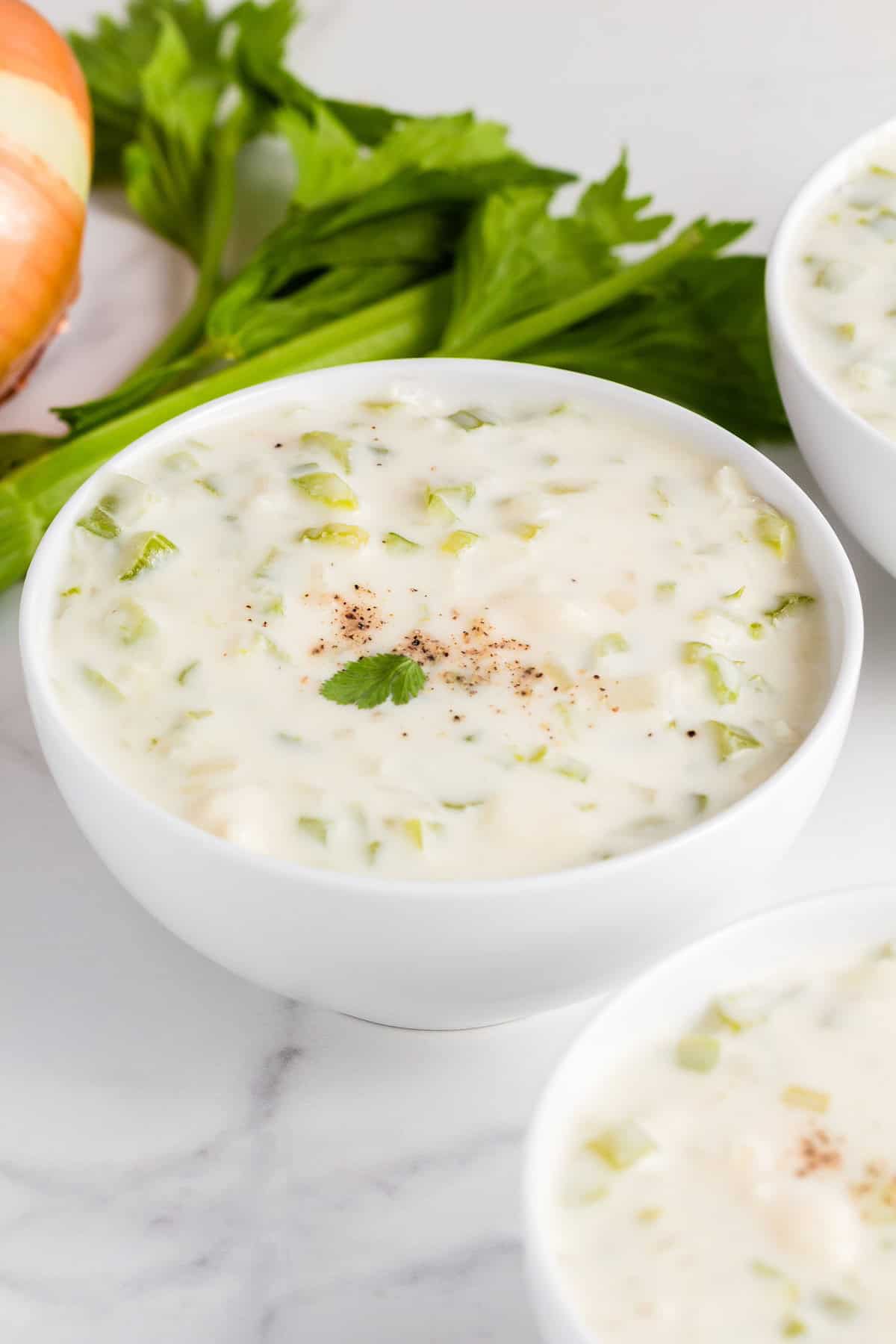 A bowl of creamy soup with celery, topped with pepper and parsley, on a white surface.
