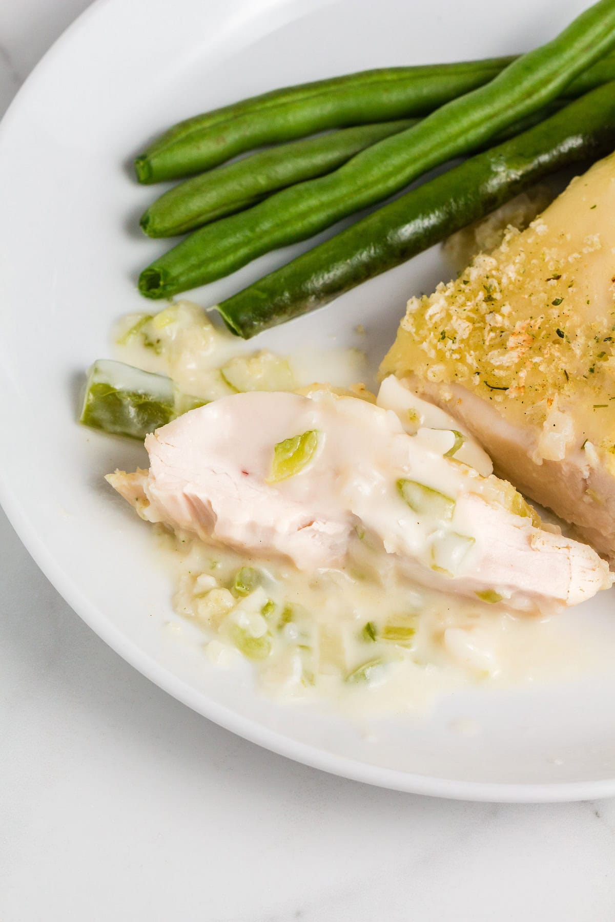 Sliced chicken with creamy sauce, green beans, and a casserole topping on a white plate.