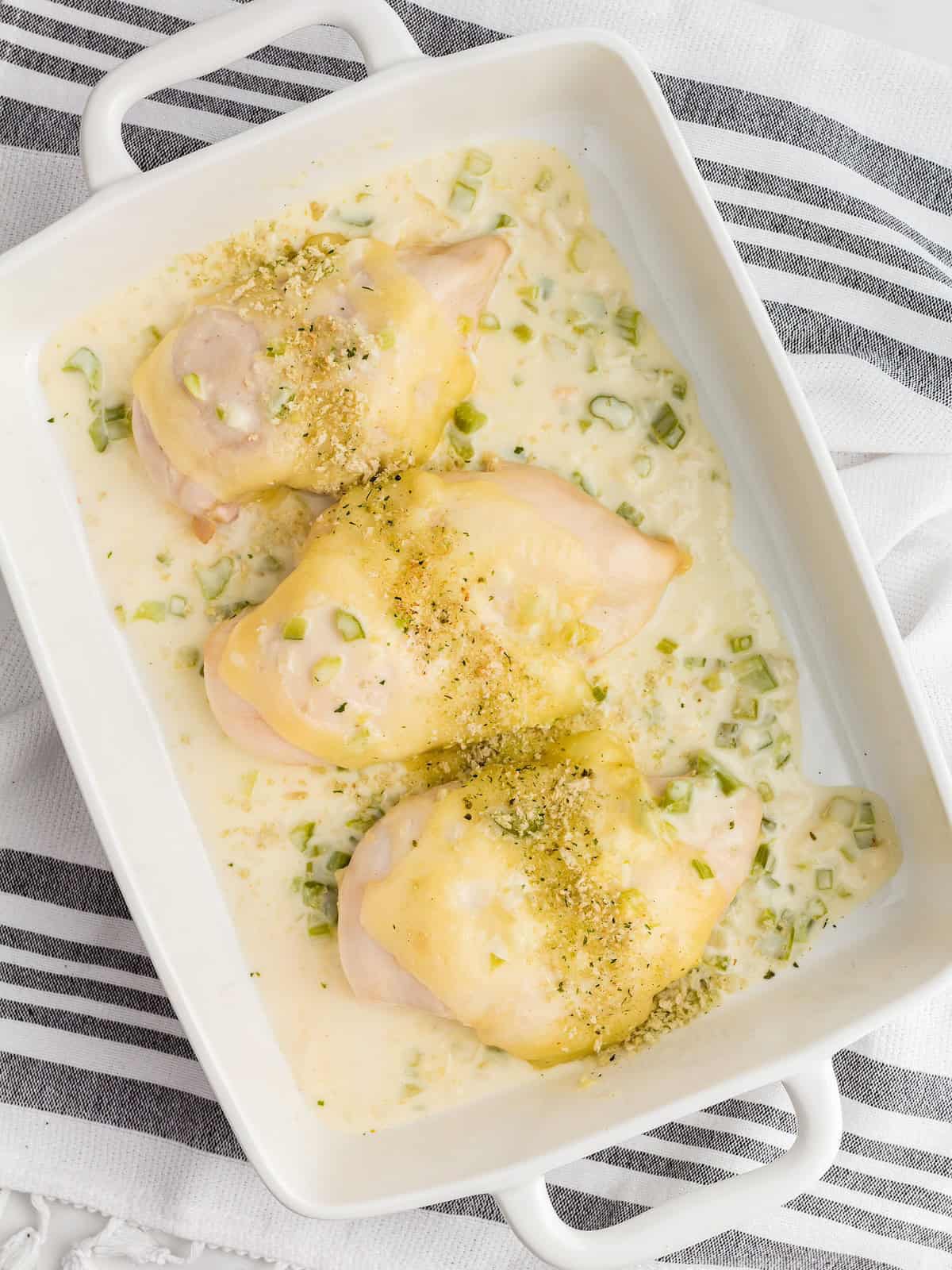 Three baked chicken breasts with sauce and herbs in a white casserole dish.