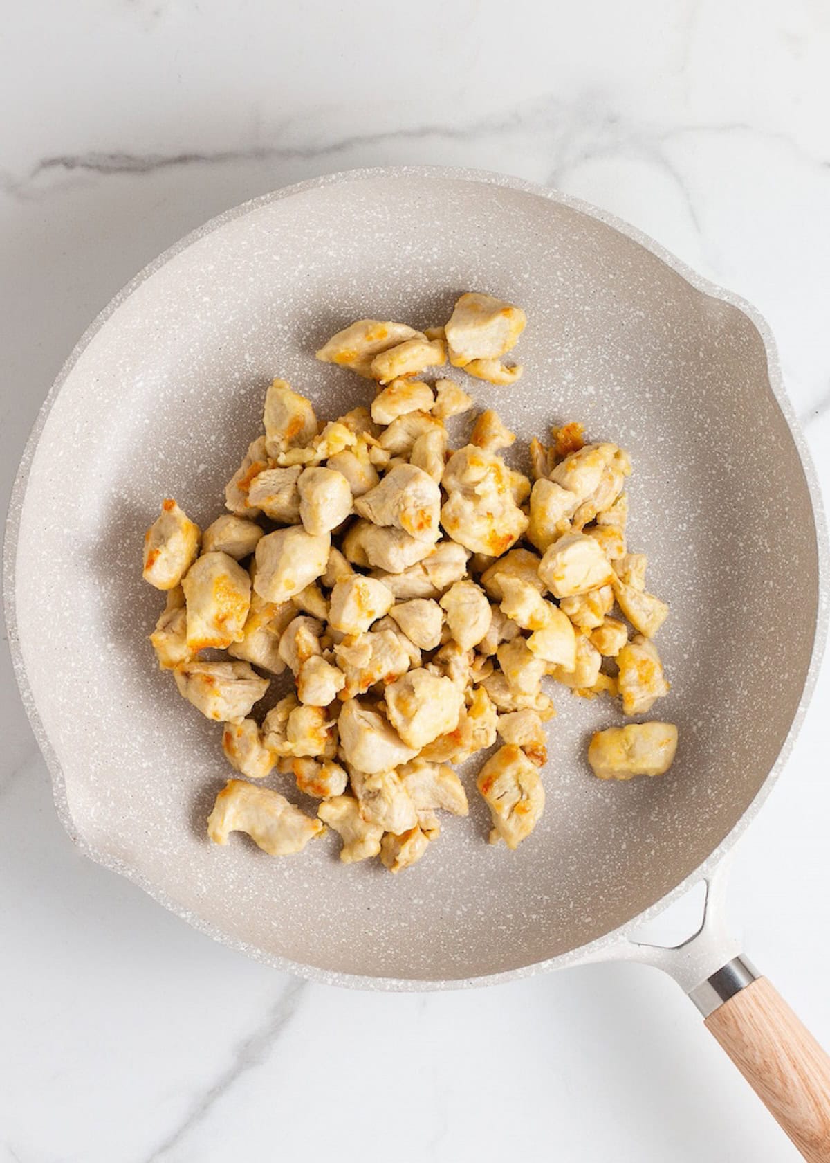 Chicken Stir Fry cooking in a light frying pan on a white marble surface.