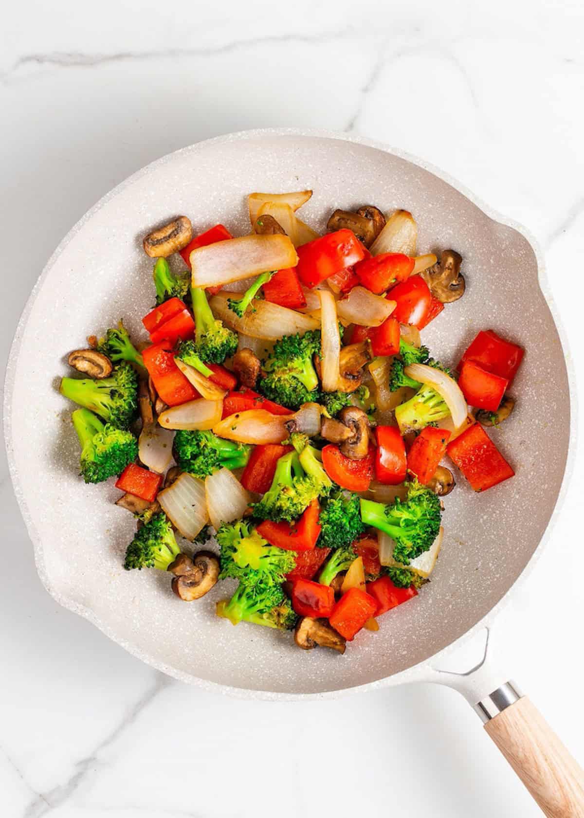 A frying pan with Chicken Stir Fry, featuring broccoli, red bell pepper, onion, and mushrooms.