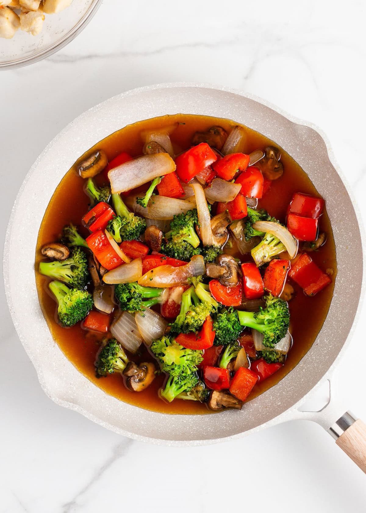 A pan of chicken stir fry with broccoli, red bell pepper, onions, mushrooms, and sauce.