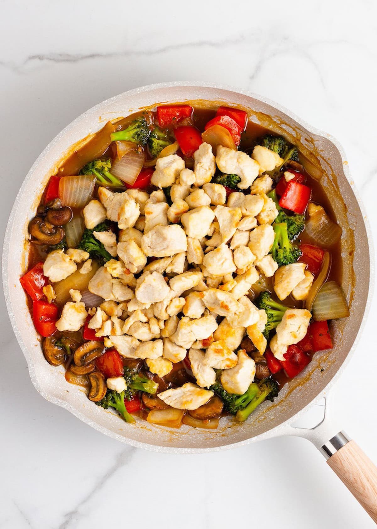 A skillet with Chicken Stir Fry-cooked chicken, broccoli, peppers, onions, mushrooms, and sauce.