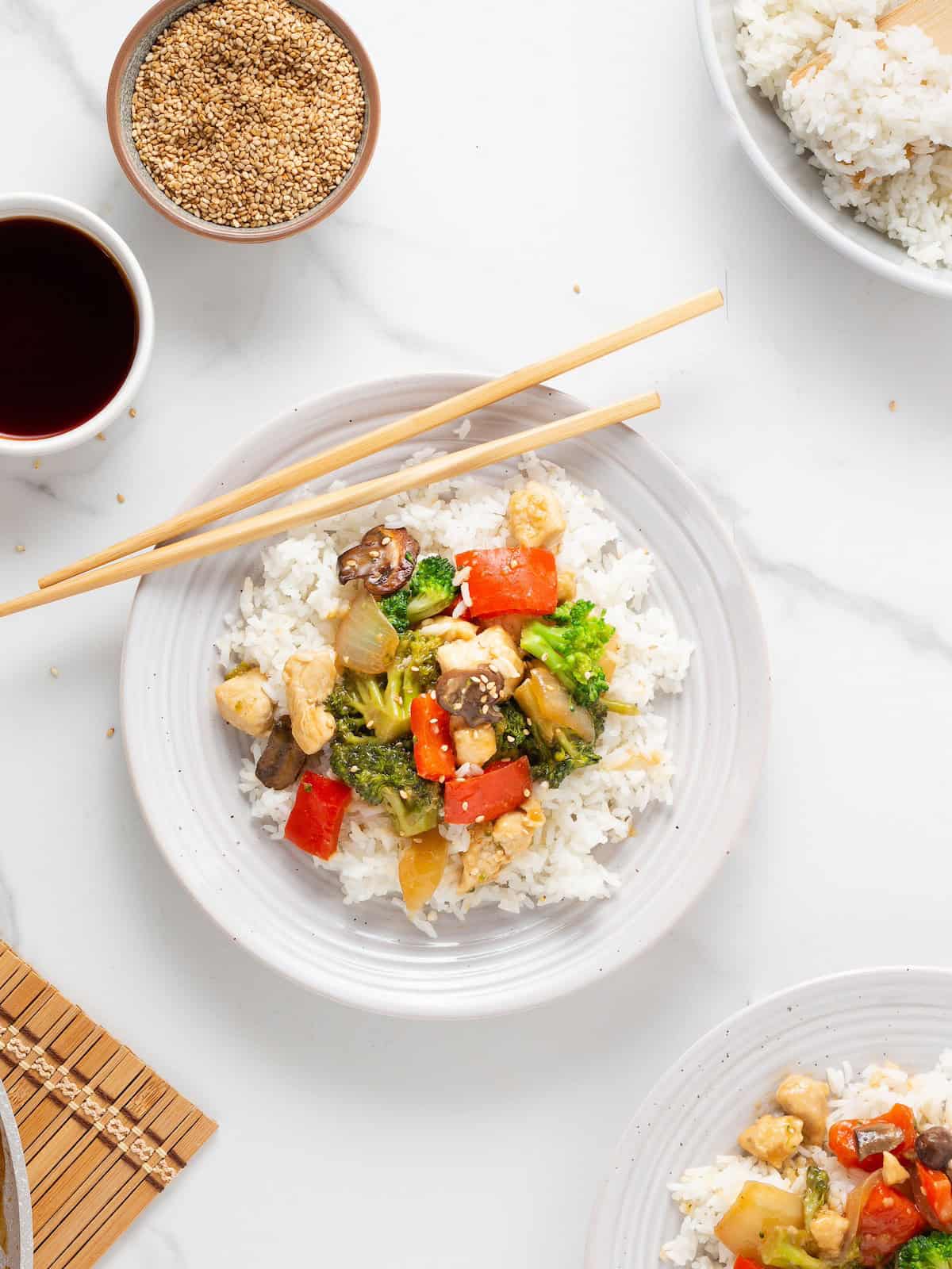 White plate with Chicken Stir Fry, rice, vegetables, and chopsticks on top.