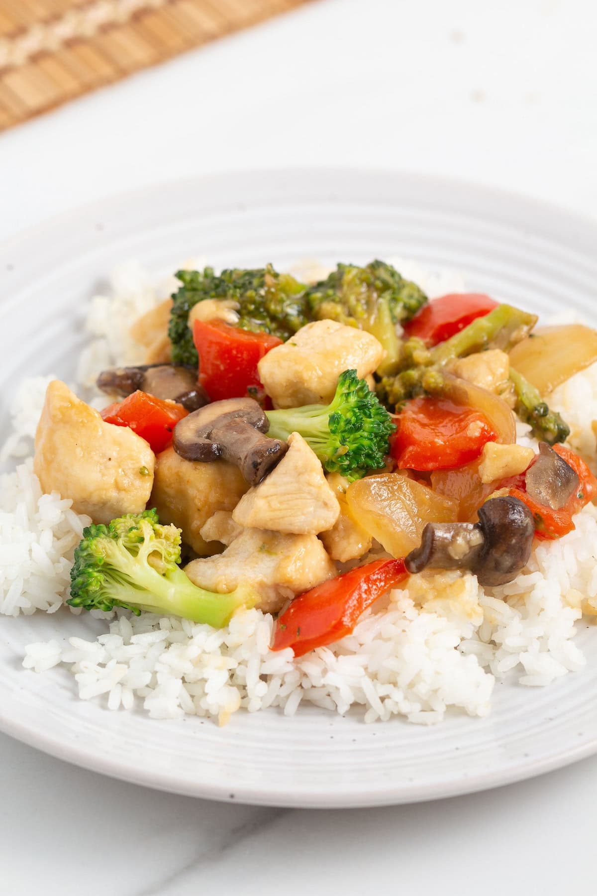 Chicken Stir Fry with broccoli, mushrooms, and peppers served over white rice on a white plate.