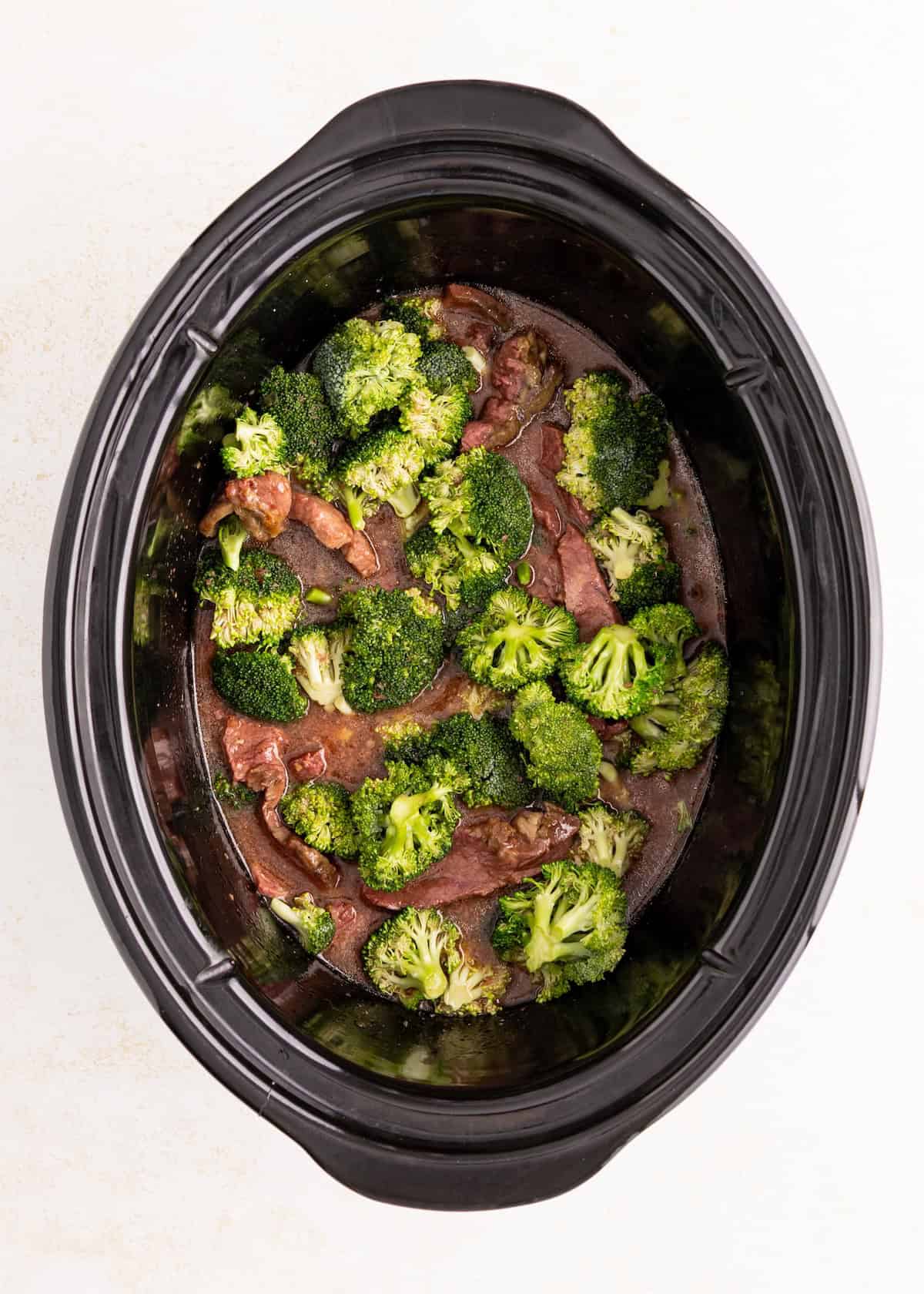 Beef and broccoli in a slow cooker with sauce, viewed from above on a white background.
