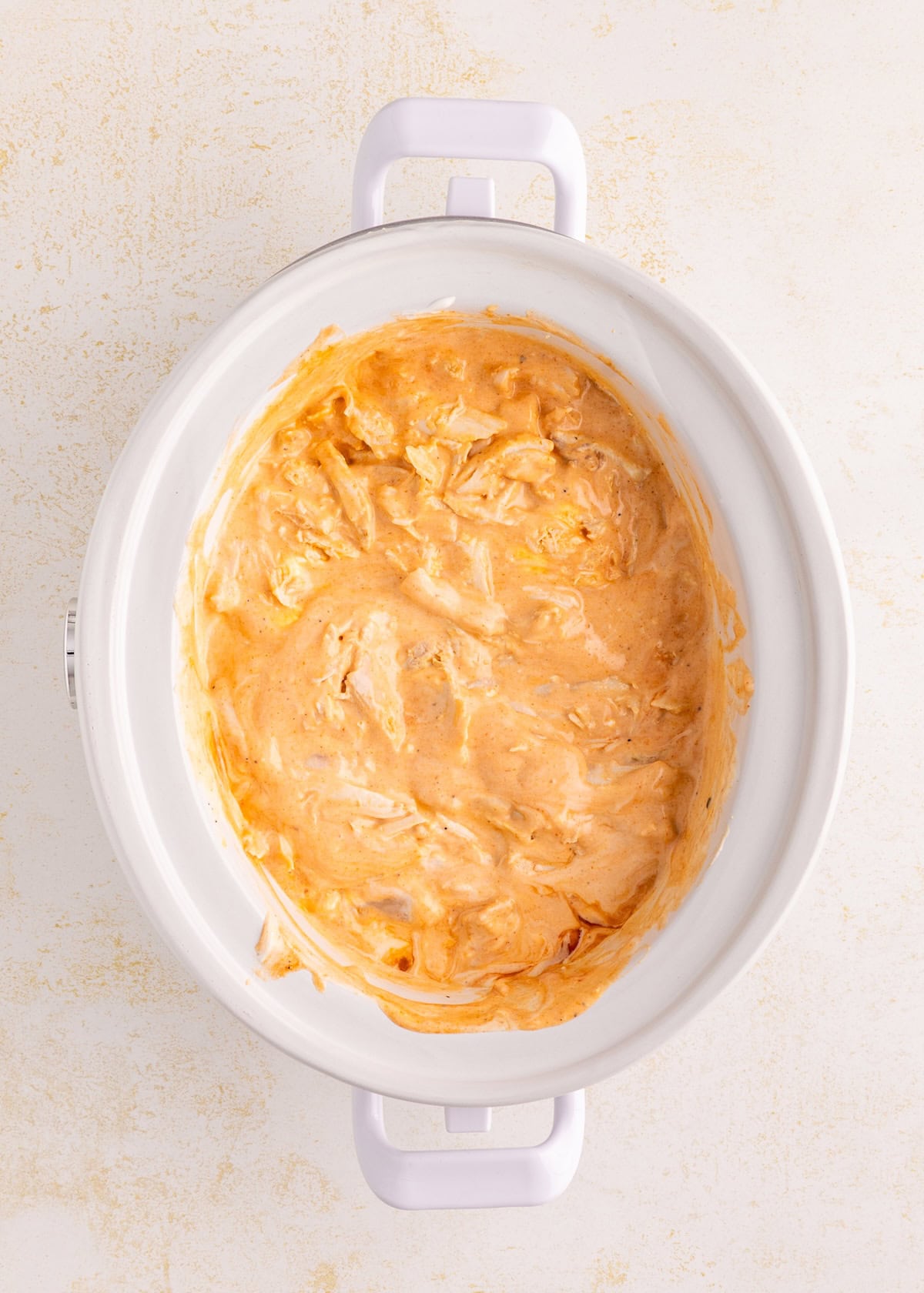 Creamy, orange dip mixture in a white slow cooker on a light background.