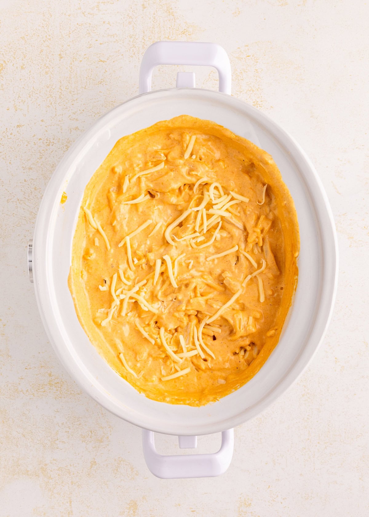Oval white baking dish with cheesy, creamy dip topped with shredded cheese.