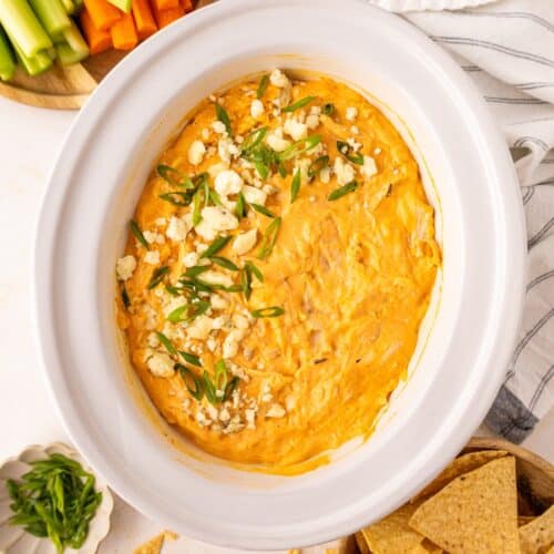 Buffalo chicken dip topped with green onions and cheese, surrounded by chips and veggies.