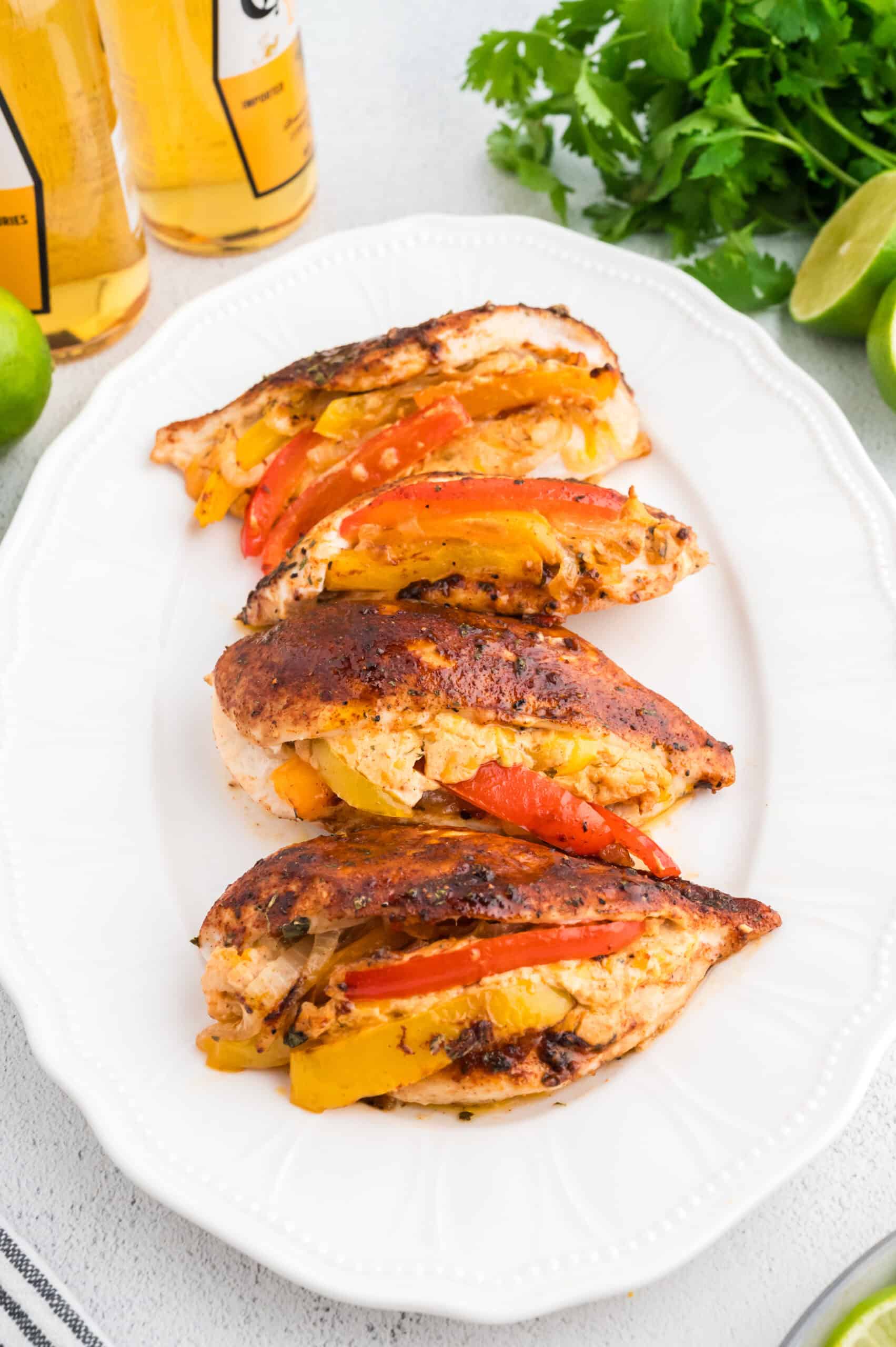 Four stuffed and seasoned chicken breasts with sliced peppers on a white oval plate.
