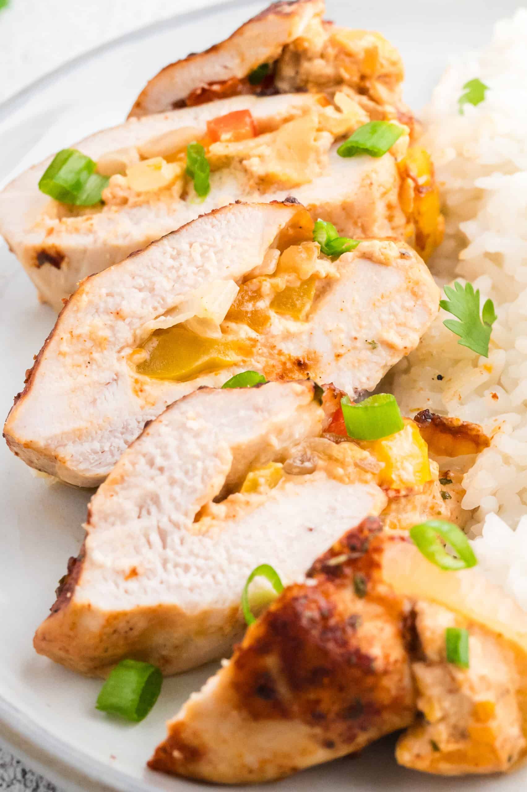 Sliced stuffed chicken breast with vegetables, served with white rice and green onions.