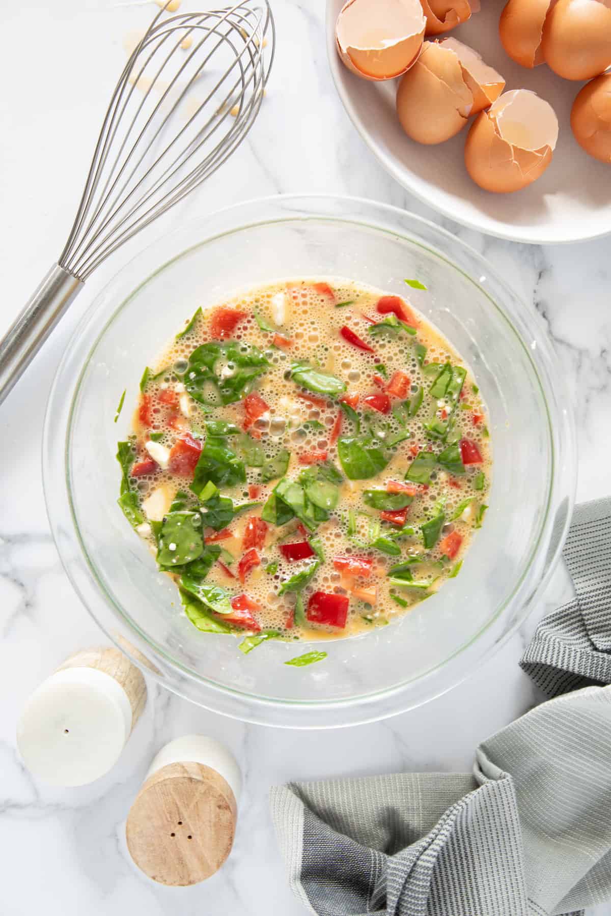 A bowl of whisked eggs with spinach, peppers-perfect for Feta Spinach Egg Muffins prep.