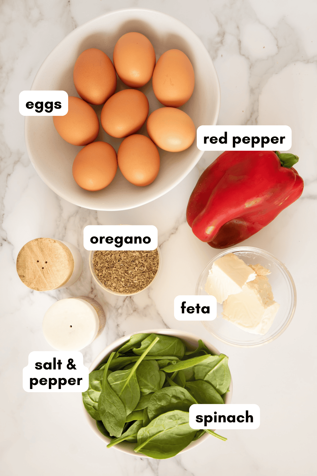 Eggs, red pepper, feta, spinach, oregano, and salt & pepper on a marble surface.