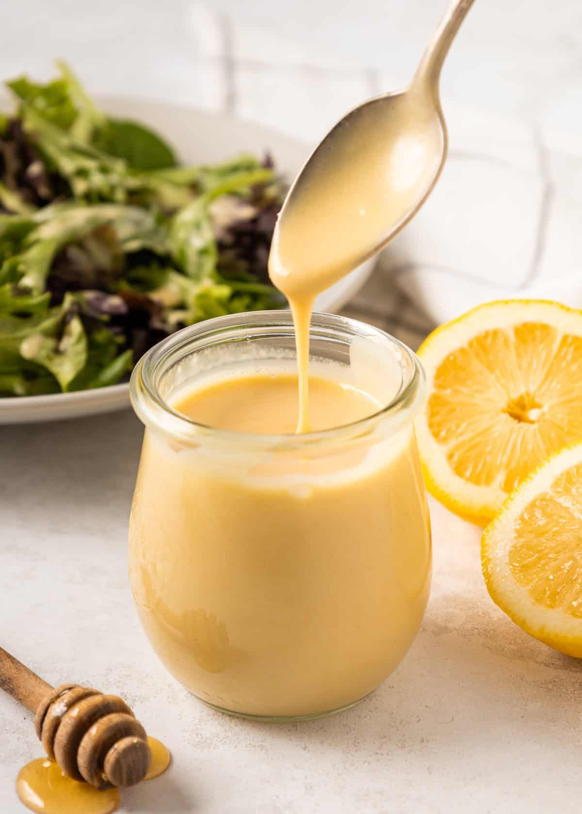 Honey Mustard Dressing drizzled into a jar, with salad greens and lemon slices on the side.