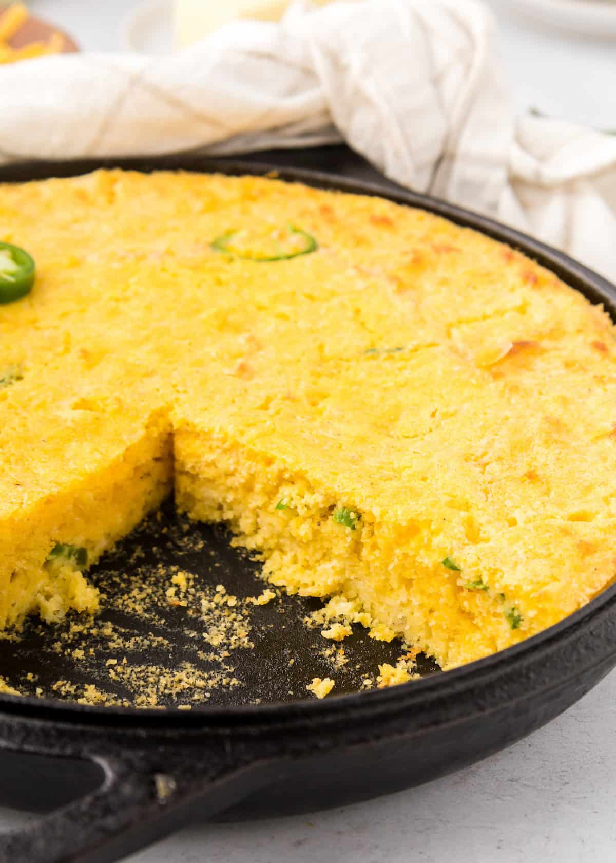 Jalapeño Cheddar Cornbread baked golden in a cast iron skillet, with one slice missing.