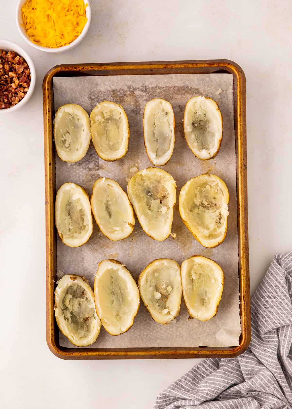 Halved baked potatoes with scooped centers on a parchment-lined baking sheet.