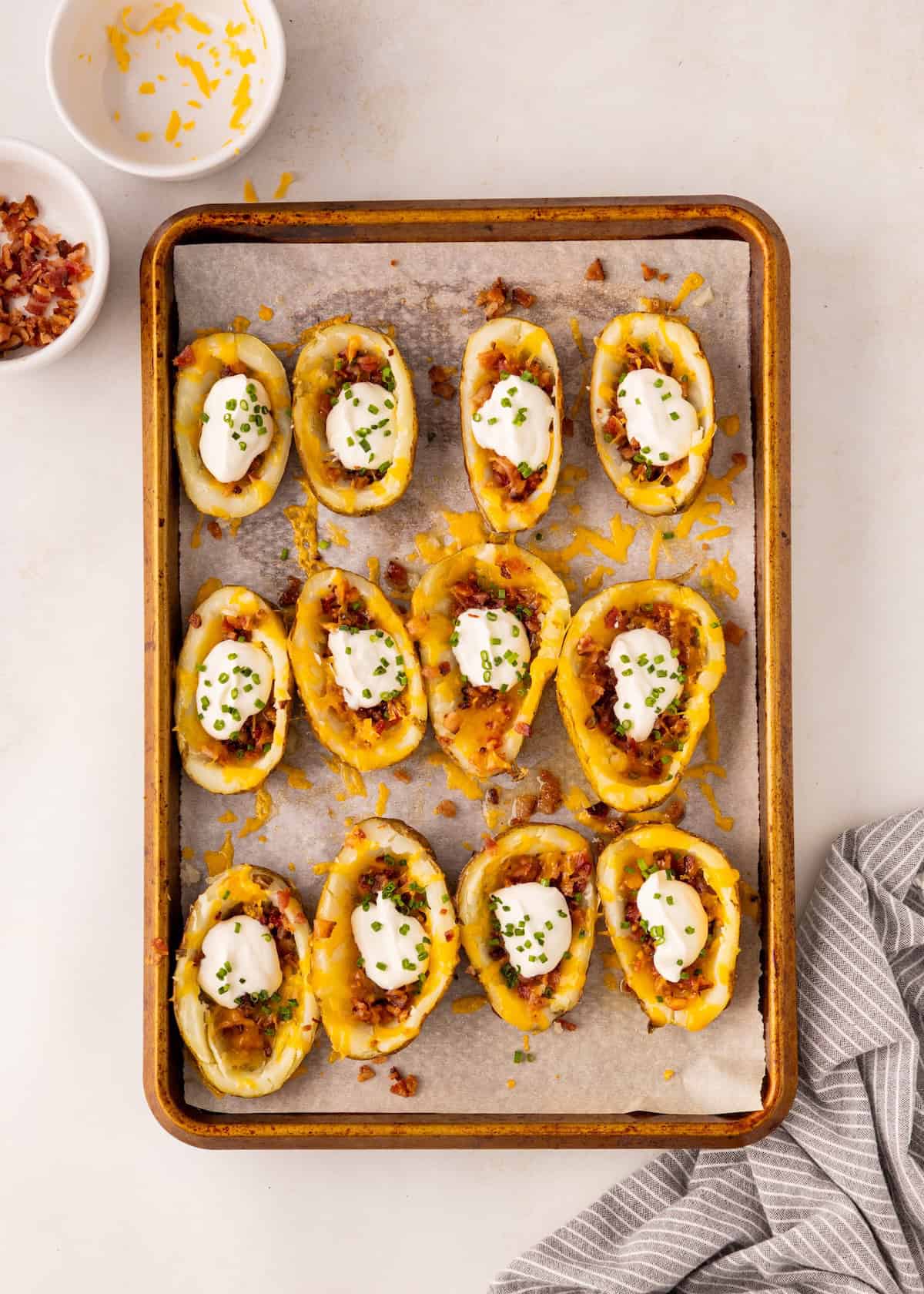 A tray of loaded potato skins topped with sour cream, bacon bits, and chopped chives.