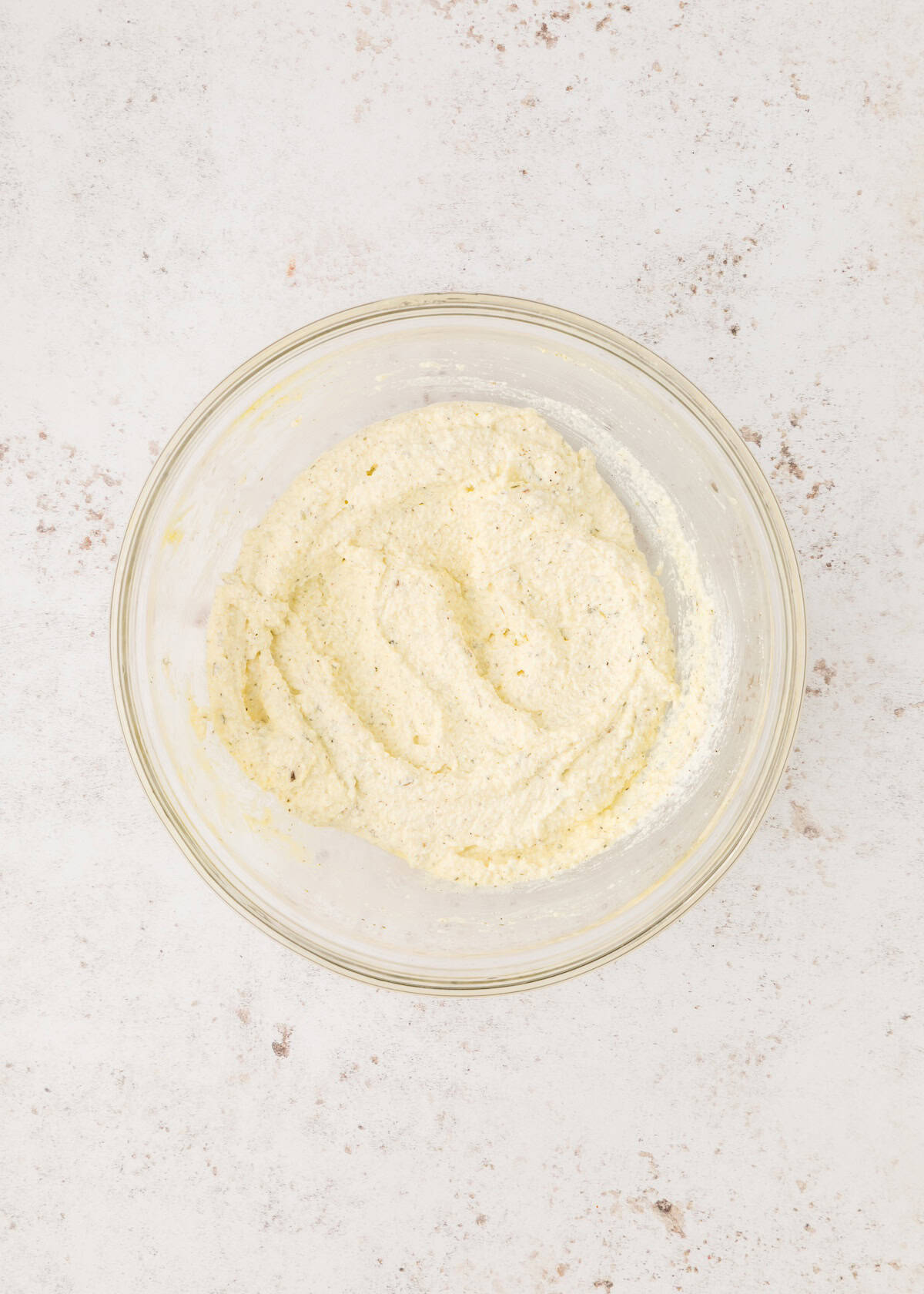 A glass bowl with a creamy, white cheese mixture on a light, textured surface.