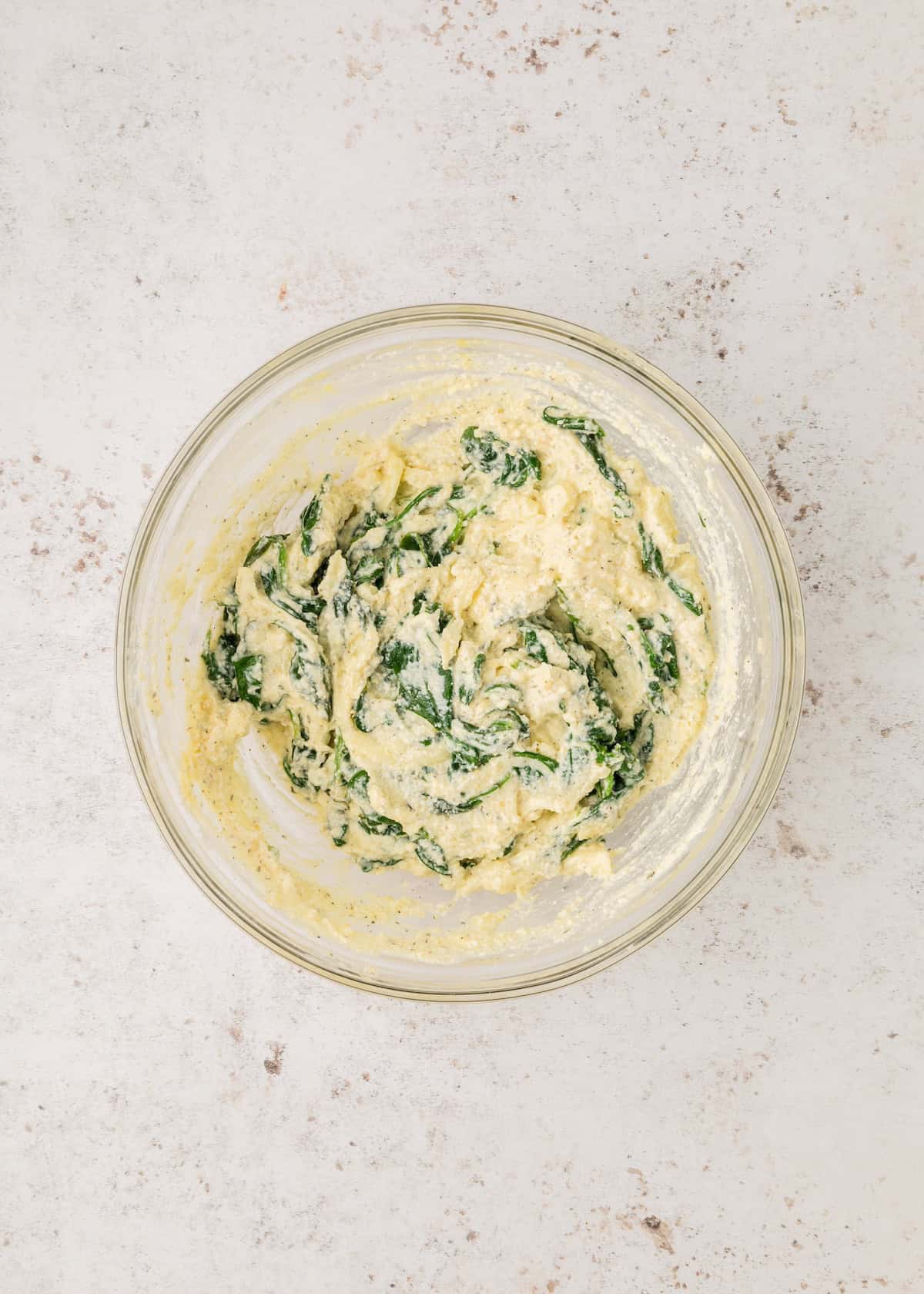 A glass bowl with ricotta and spinach mixture on a light, textured surface.