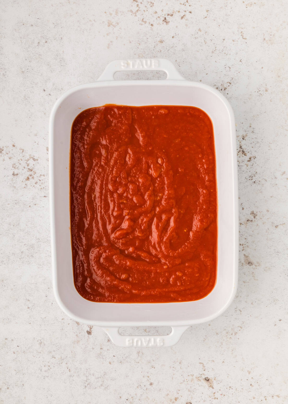 Rectangular white dish filled with red tomato sauce on a light textured surface.