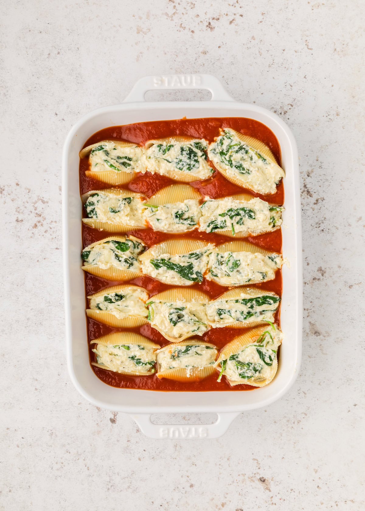Stuffed pasta shells with spinach and cheese in tomato sauce in a white baking dish.