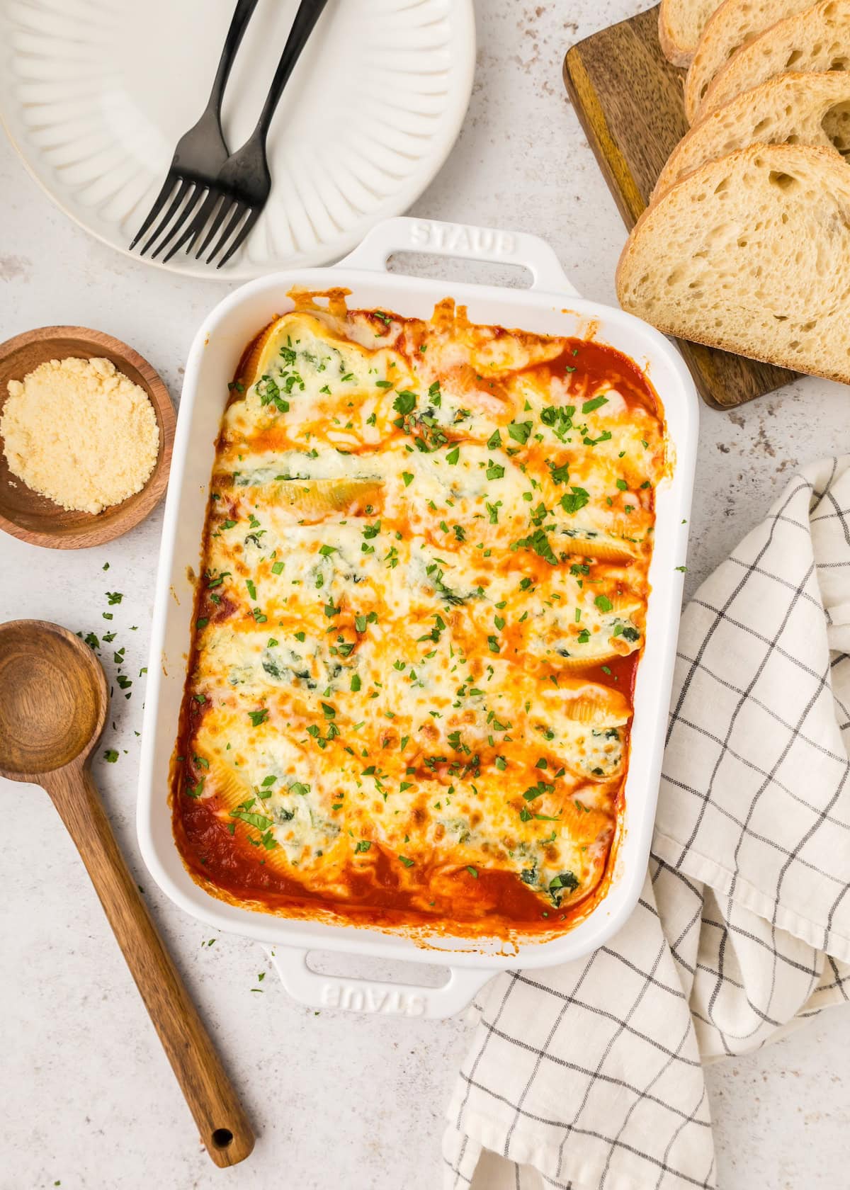 Baked stuffed pasta shells with cheese and herbs in a white dish, with bread slices nearby.