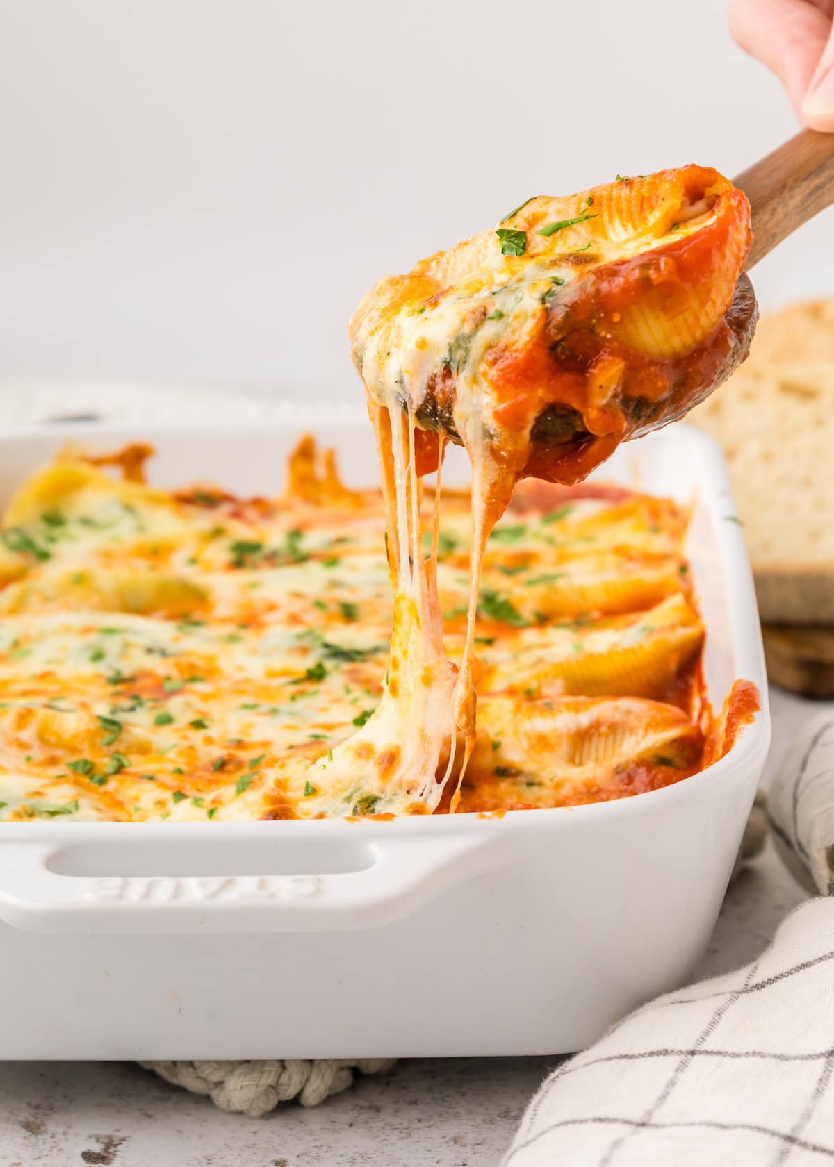 A cheesy stuffed pasta shell is being lifted from a baked dish with melted cheese stretching.