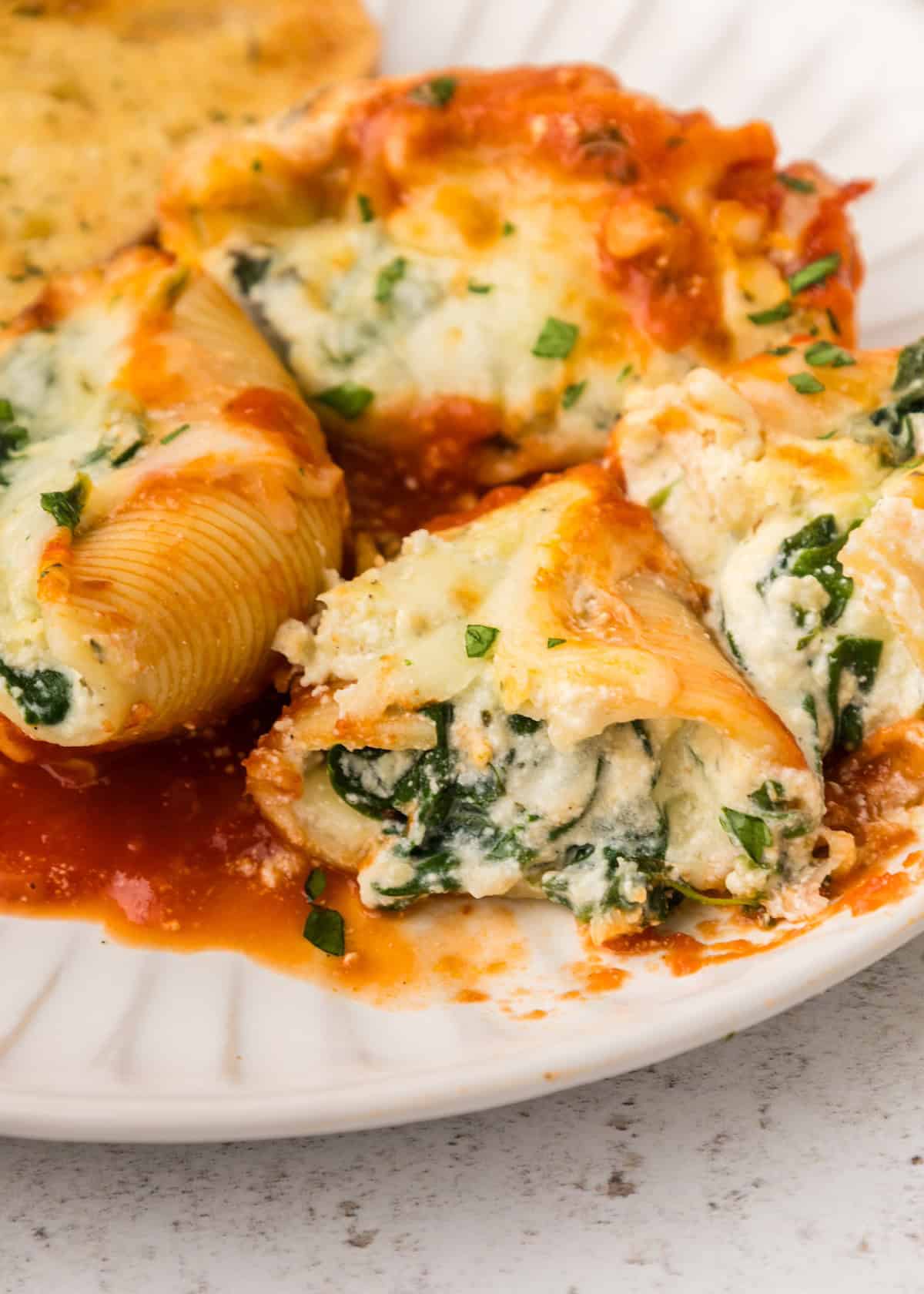 Stuffed pasta shells with spinach and cheese filling in tomato sauce on a white plate.