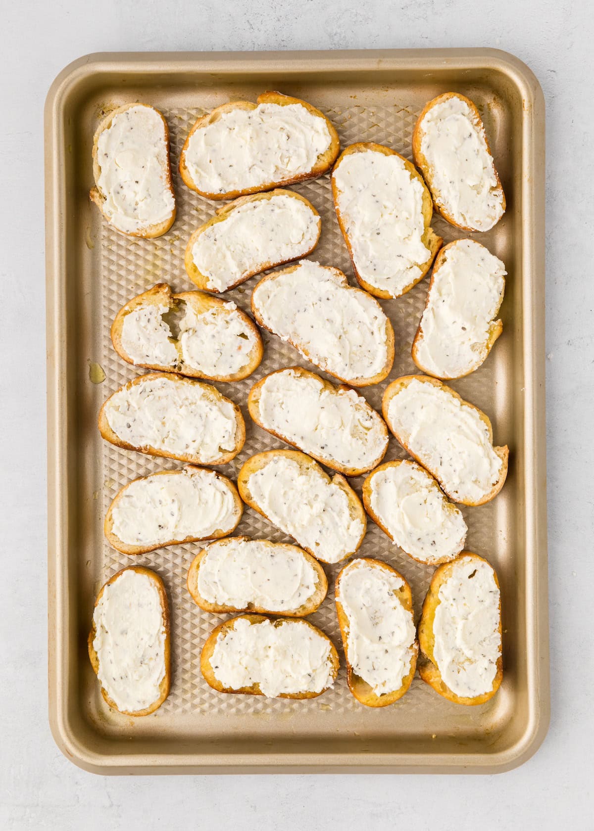 Sliced bread with a creamy spread arranged on a baking sheet.
