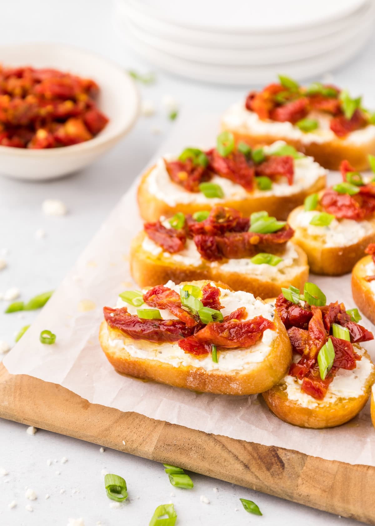 Toasted bread with creamy spread, sun-dried tomatoes, and chopped green onions on top.