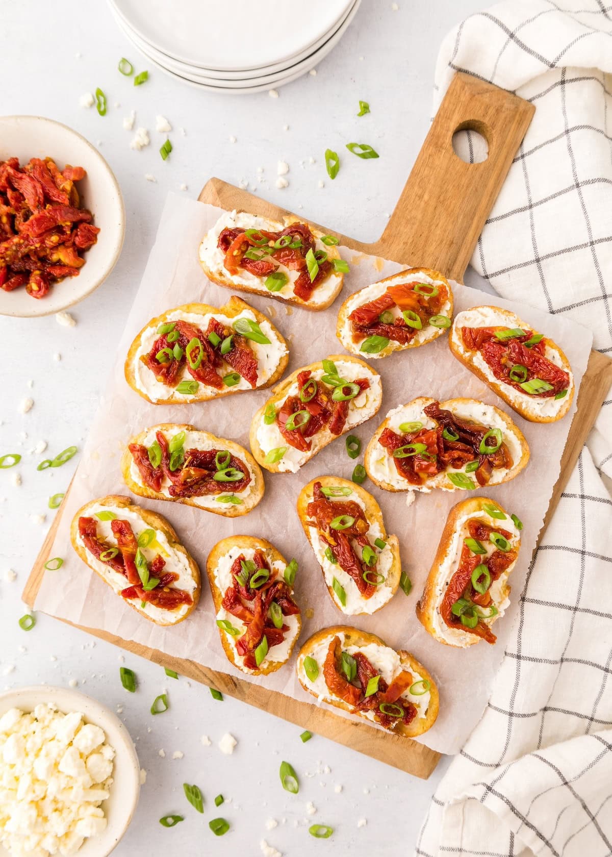 Toasted bread slices with cheese, sun-dried tomatoes, and green onions on a wooden board.