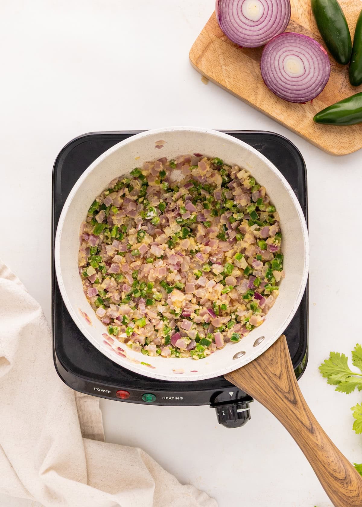 Chopped onions and peppers sautéing in a pan on a stovetop, with vegetables on the side.