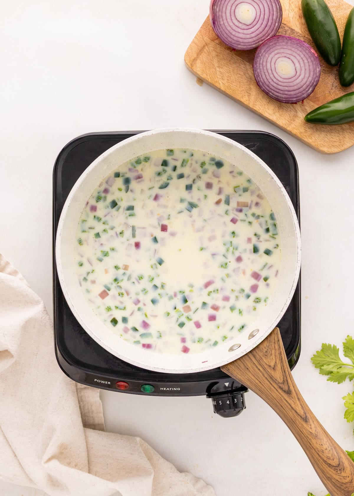 A pan of creamy soup with chopped red onions and green peppers on a stovetop.