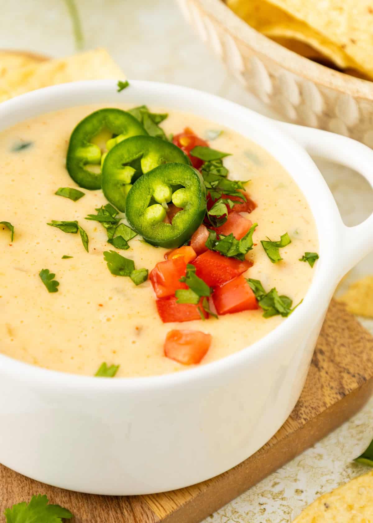 Creamy cheese dip topped with jalapeño slices, diced tomatoes, and cilantro in a white bowl.