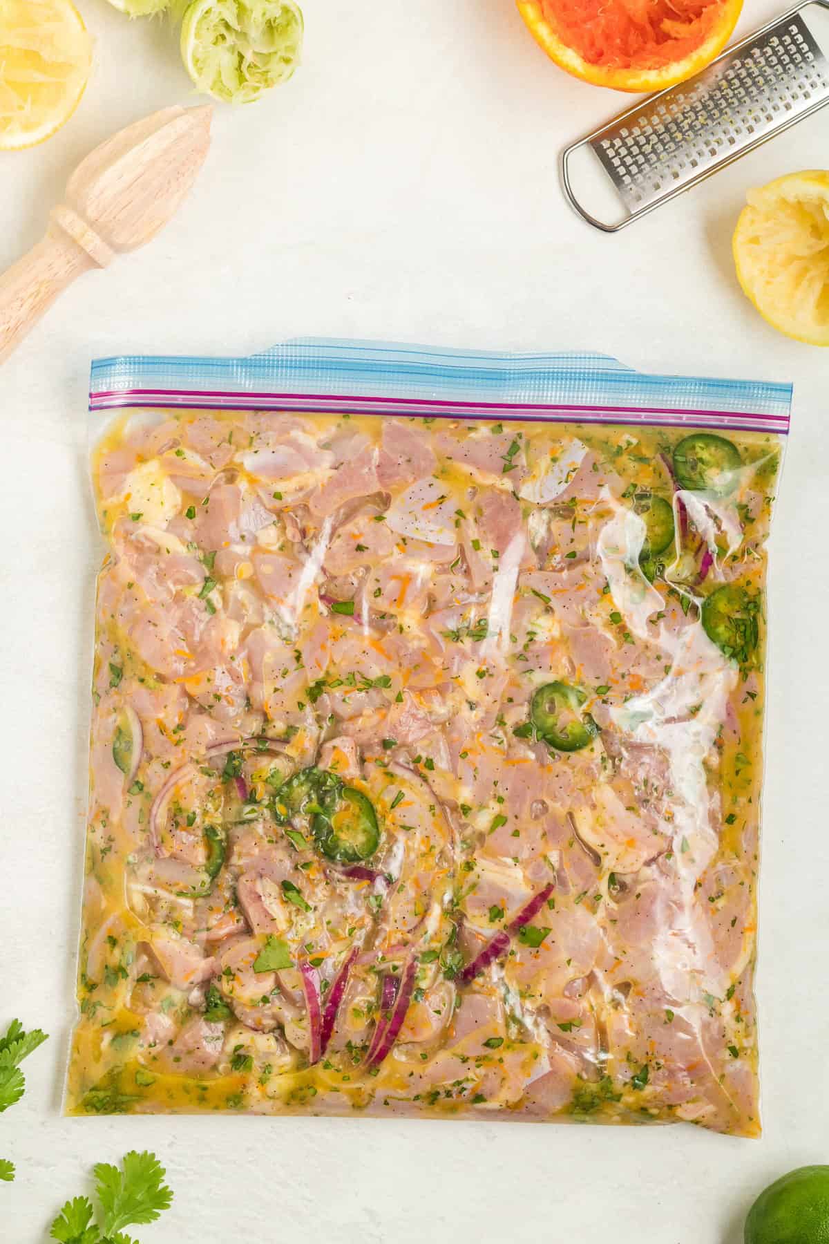 Raw marinated chicken in a ziplock bag surrounded by citrus fruits and kitchen tools.