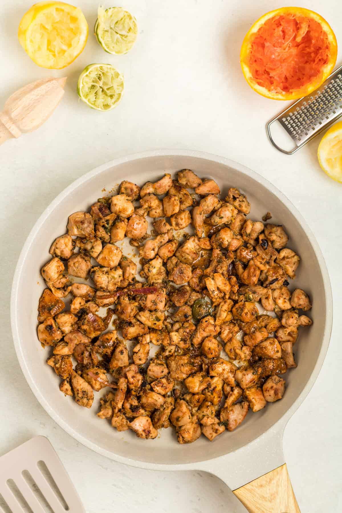 Cooked, seasoned chicken pieces in a skillet with squeezed citrus fruits nearby.