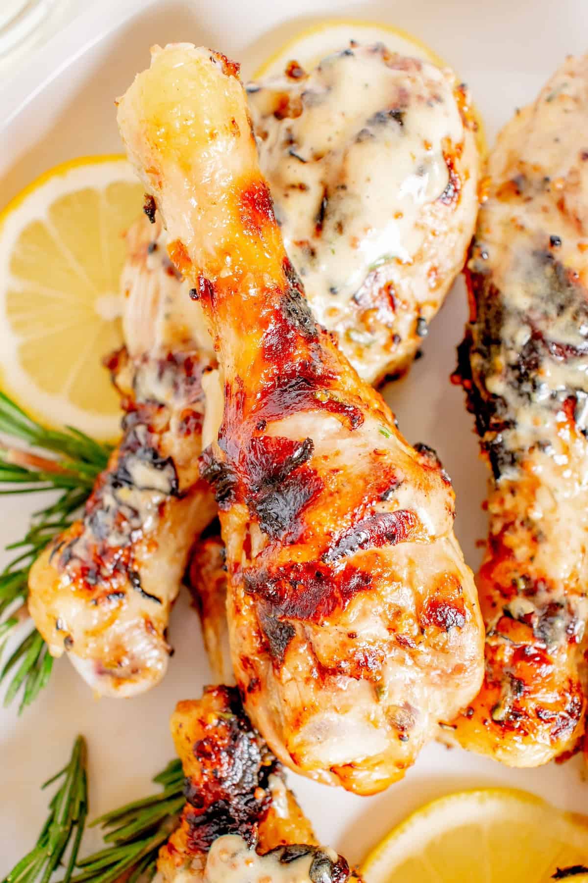 Grilled chicken drumsticks with herbs, lemon slices, and rosemary on a white plate.