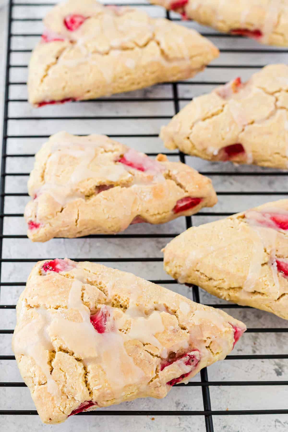 Strawberry scones with glaze cooling on a black wire rack.
